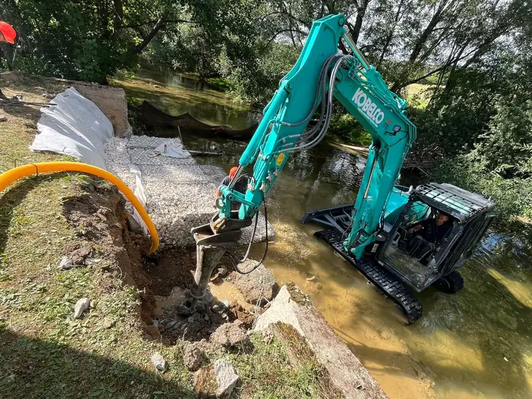 Pelle mécanique dans le lit d’une rivière consolidant une berge protégée par un enrochement en gabion